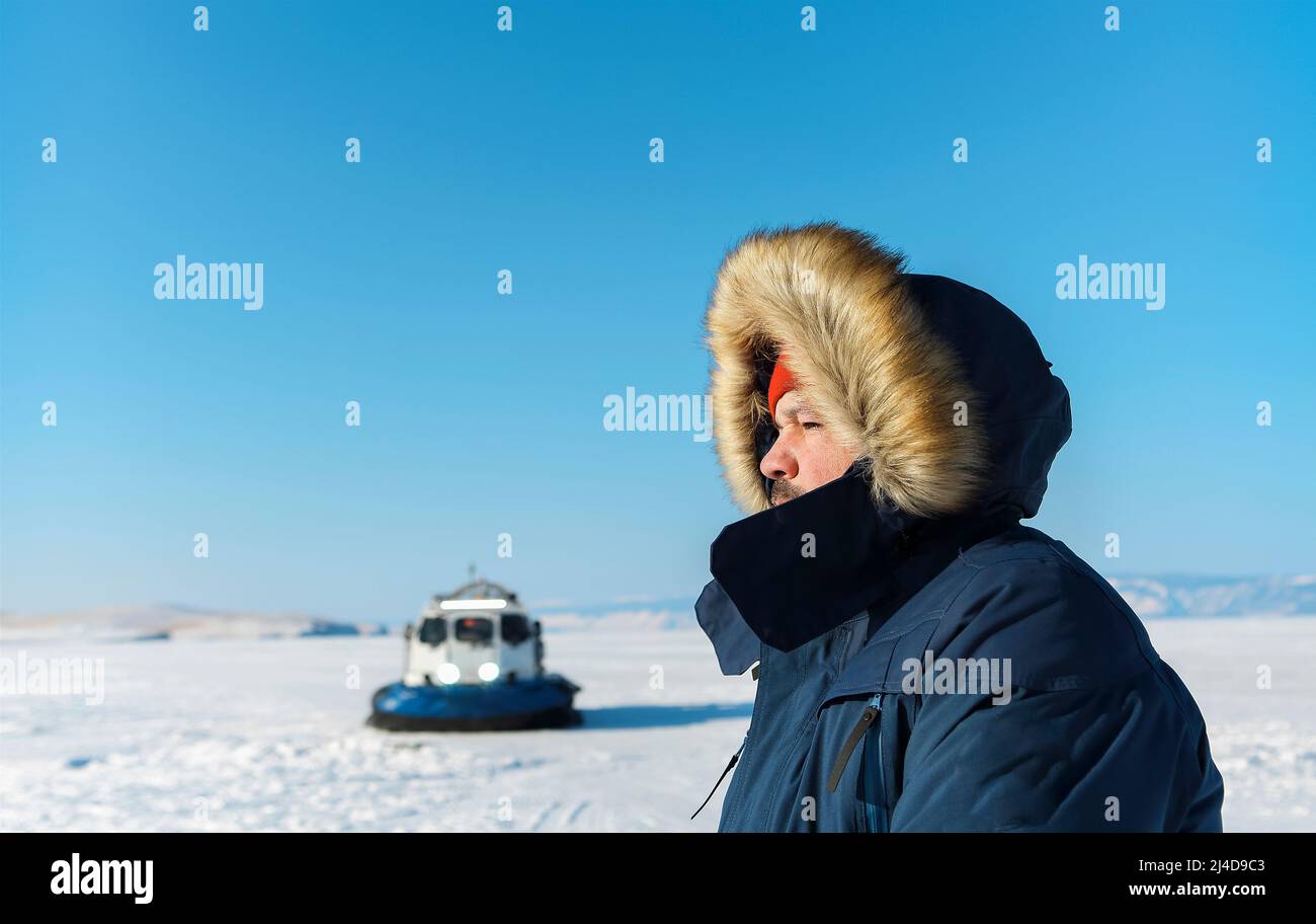 Portrait of the man wearing eyesglasses and winter clothes standing by Khivus. Transport on ice. On the surface of the transparent frozen Lake Baikal. Stock Photo
