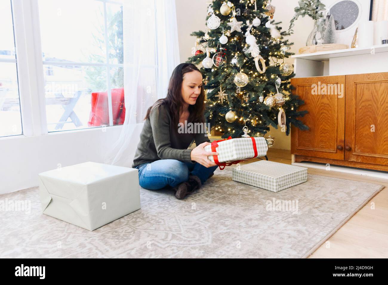 Happy young caucasian woman packing presents at home under decorated christmas tree. Smiling girl in a knitted sweater celebrating the new year. Happy Stock Photo