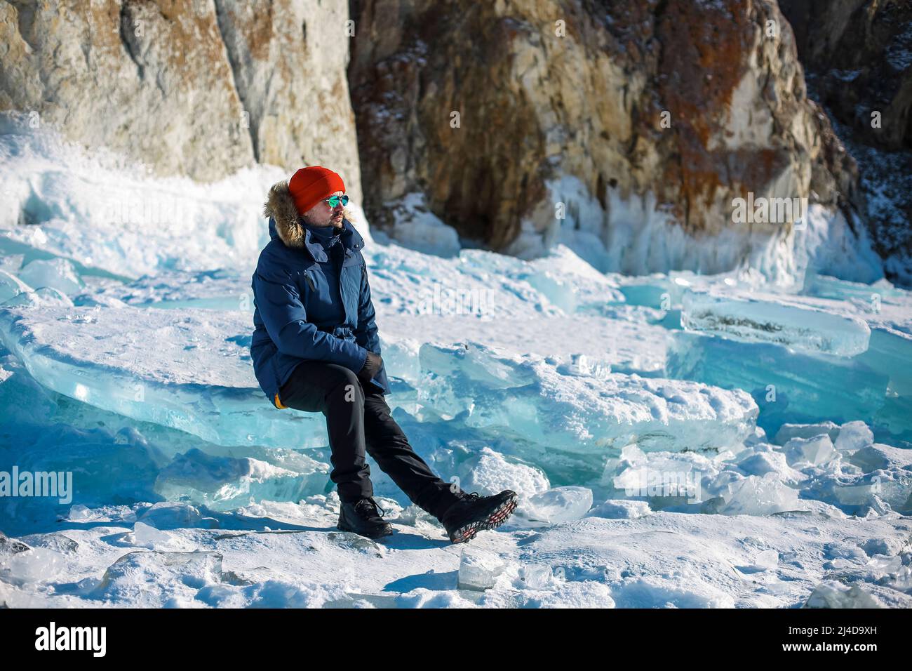 Travel and winter holiday. Lake Baikal. Portrait of the man tourist in red cap and blue jacket wearing sunglasses on ice Stock Photo