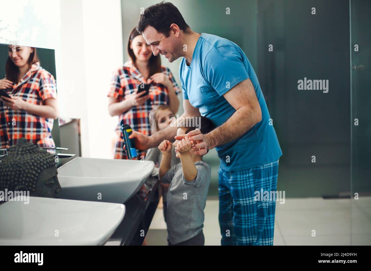 Caucasian parents and three kids in pajamas having morning routine in bathroom, standing near the mirror, smiling after brushing teeth. Family vacatio Stock Photo
