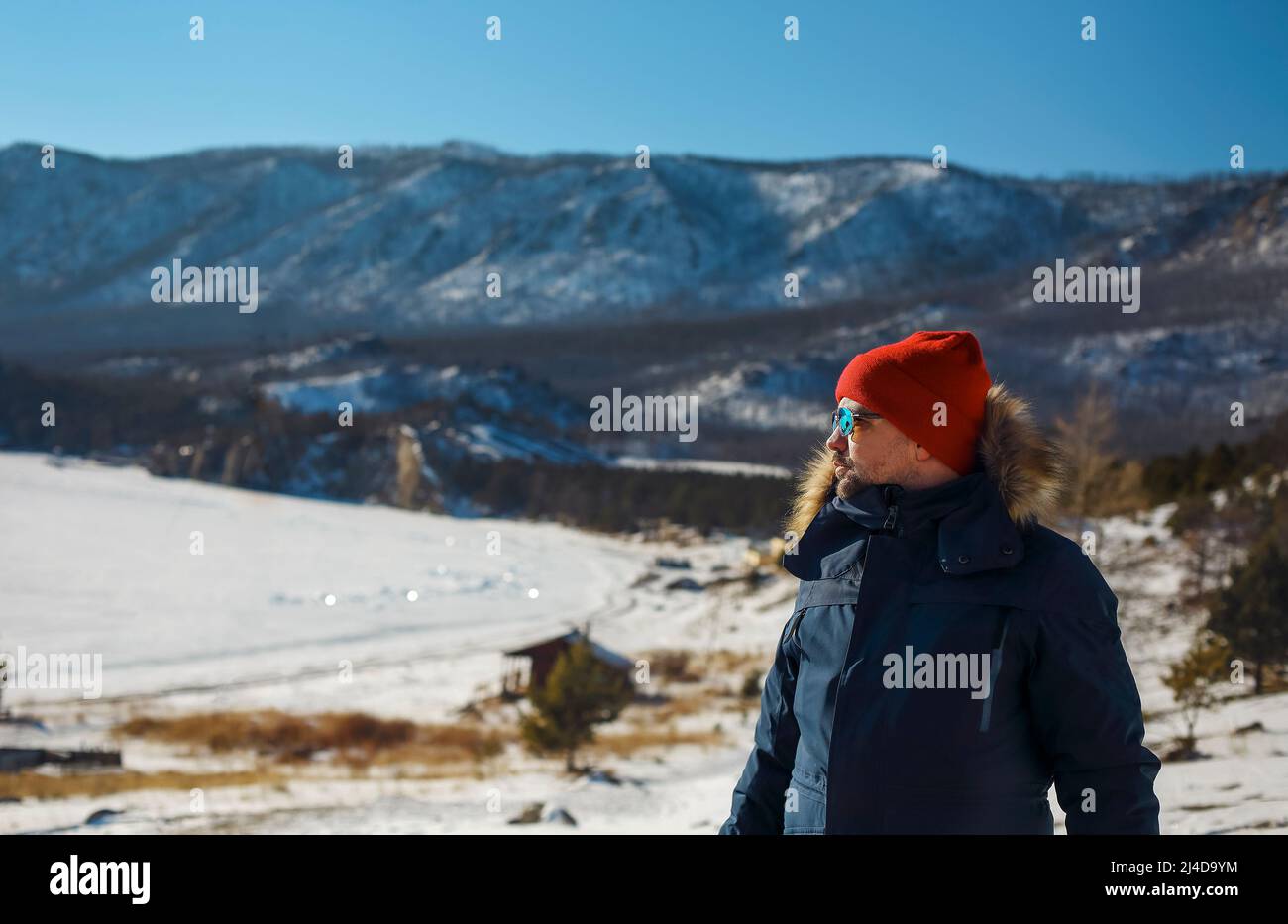 Traveller man in a blue winter jacket ad red cap in the woods. Sandy bay, Baikal lake, winter time. Travel and adventure concept Stock Photo