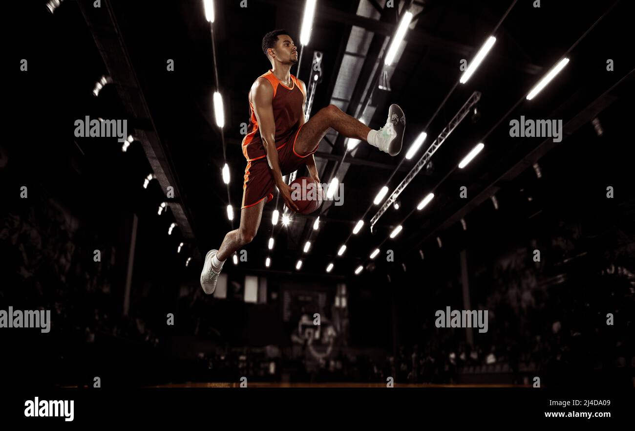 In action. Young basketball player jumping with ball in flashlights