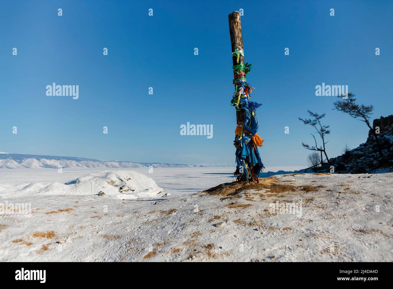 Lake Baikal in winter. Beautiful rocky island on a background of blue sky and ice. Traditional buryat shaman sacred pillar with colorful ribbons in wi Stock Photo