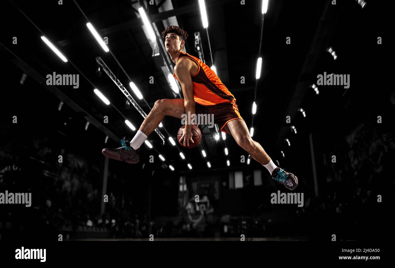 In action. Young basketball player jumping with ball in flashlights