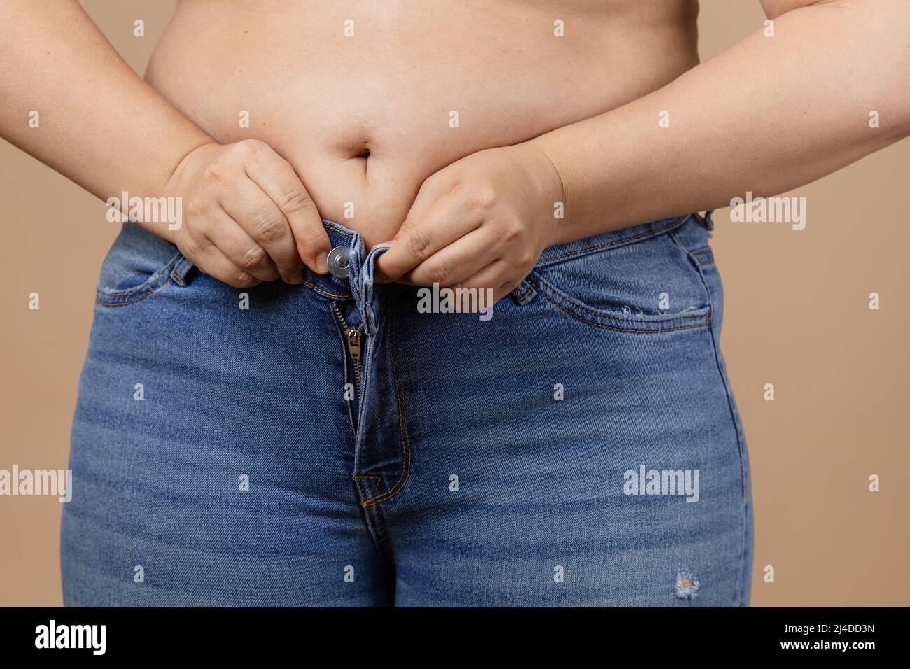 Caucasian female with big belly and overweighted sides trying to zip up blue jeans. Visceral fat. Body positive. Sudden weight gain. Tight little Stock Photo