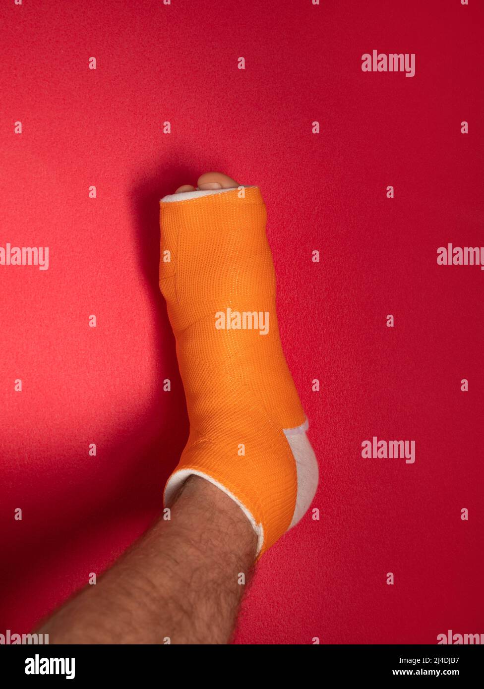 Foot with broken toe bone in orange fiberglass cast pink background