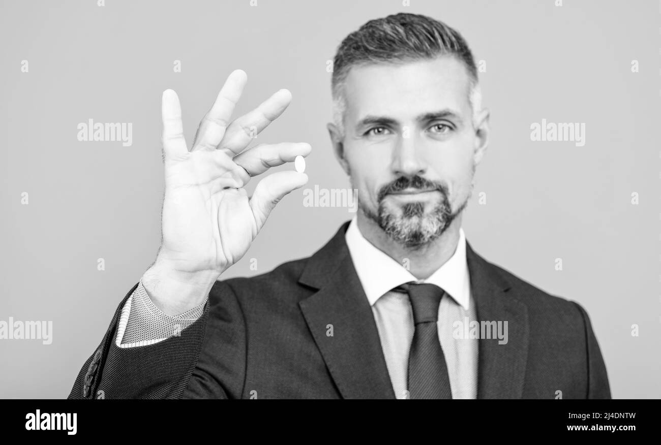 mature business man with grizzled hair in suit hold pill in hand with ok gesture, energy remedy Stock Photo