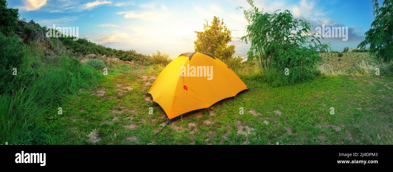 Panorama of a hill with orange tourist tent on top Stock Photo