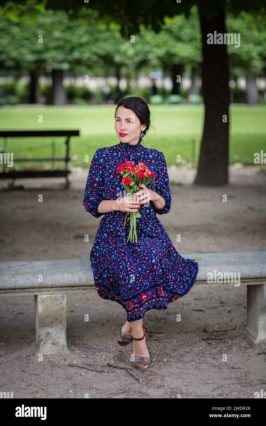 Attractive woman in a blue dress sitting in the park Stock Photo - Alamy