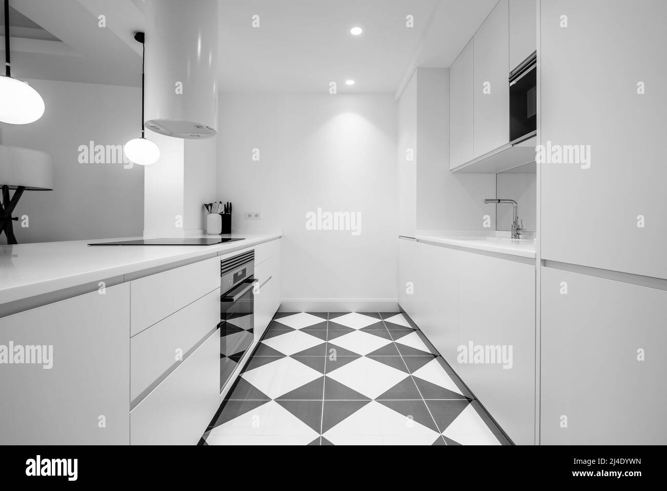 Kitchen with white wooden cabinets, straight lines and integrated appliances, gray and white floors and white hood Stock Photo