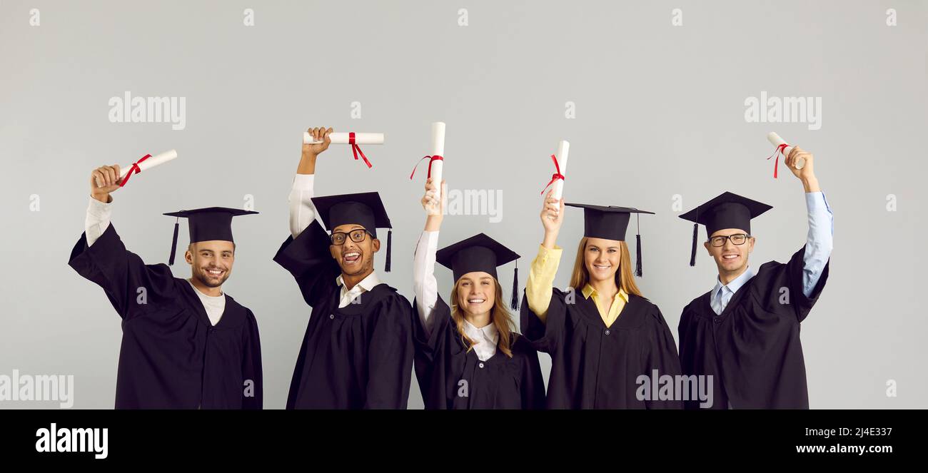 Happy diverse college or university graduates in caps and gowns holding up their diplomas Stock Photo