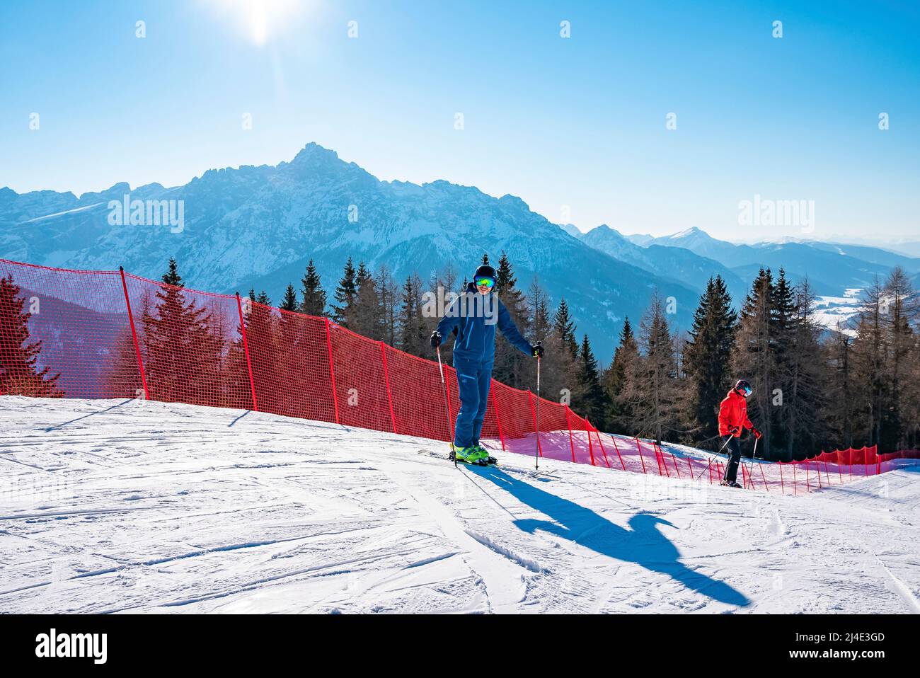 Happy skiers skiing by barrier on snow covered mountains against clear blue sky Stock Photo