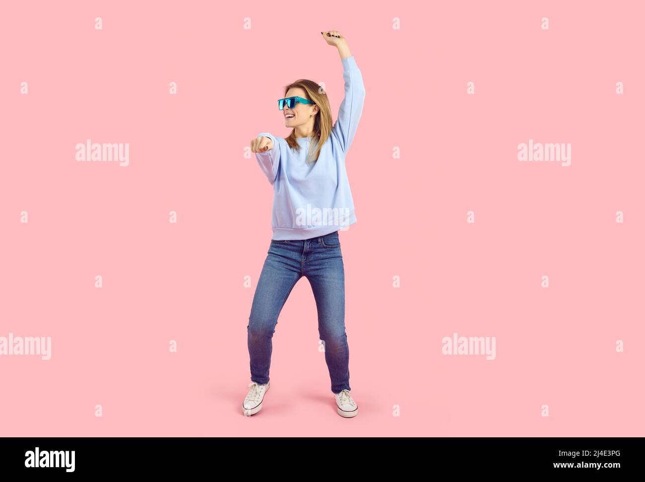 Happy young woman in casual clothes and sunglasses dancing on pink studio background Stock Photo