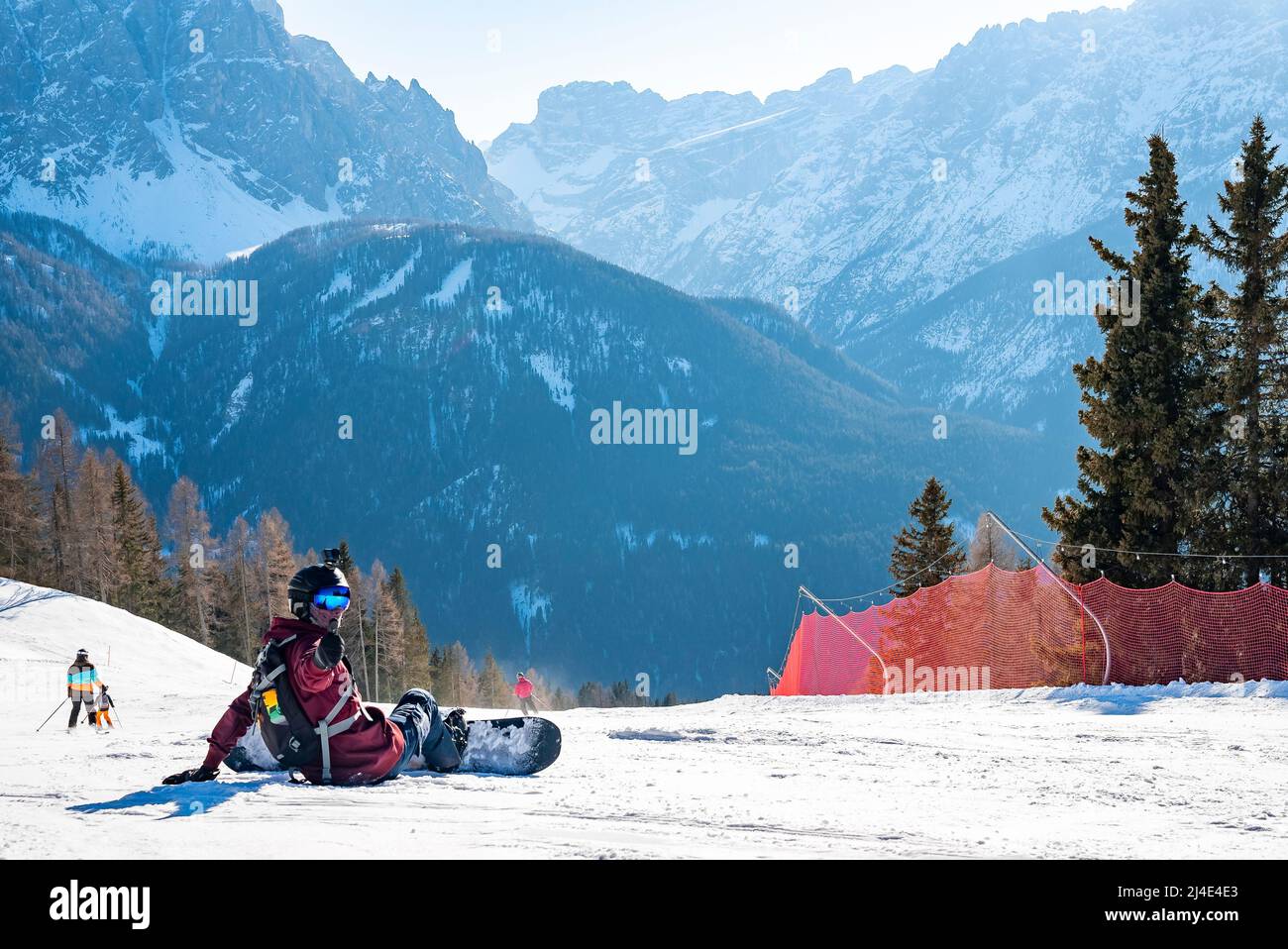 Portrait of snowboarder gesturing thumbs up while sitting on snowy landscape Stock Photo