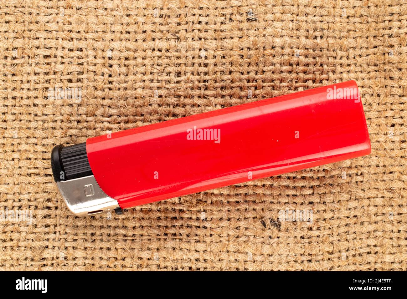 One red lighter on jute fabric, macro, top view. Stock Photo