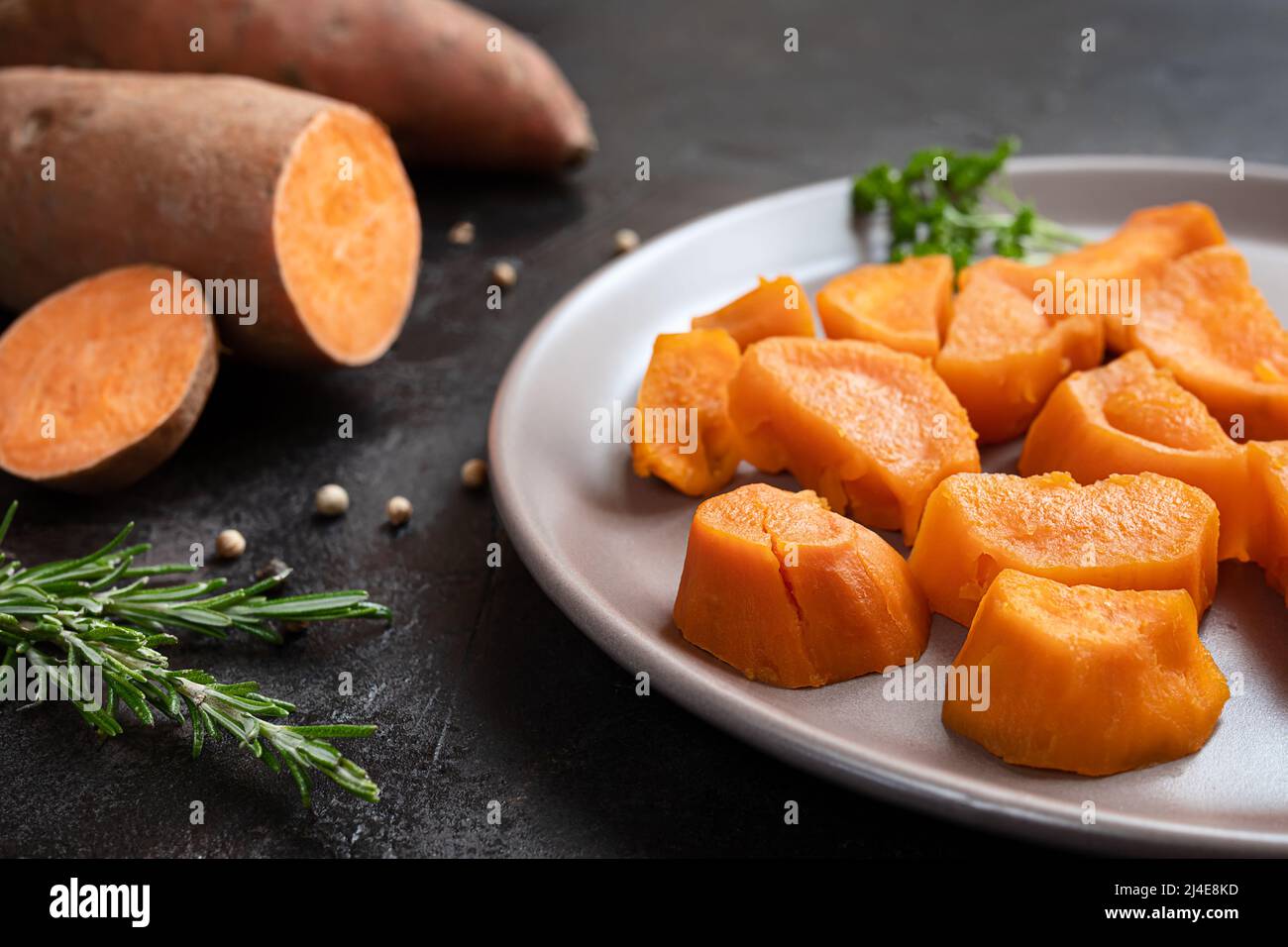 Roasted sweet potatoes and raw yam on a dark table close-up, plant based dining concept Stock Photo