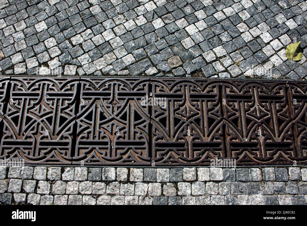 Cast iron grille over the drain. Cast iron grille over the drainage channel. Storm water drain grill on a stone sidewalk. Stock Photo