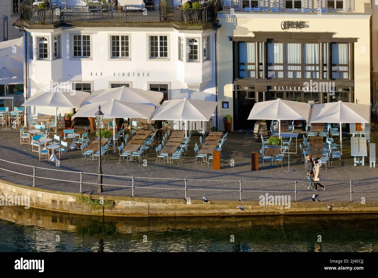 Lucerne, Switzerland - May 06, 2016: In the morning light, you can see two adjoining cafes with tables outside the buildings near the banks of the Reu Stock Photo