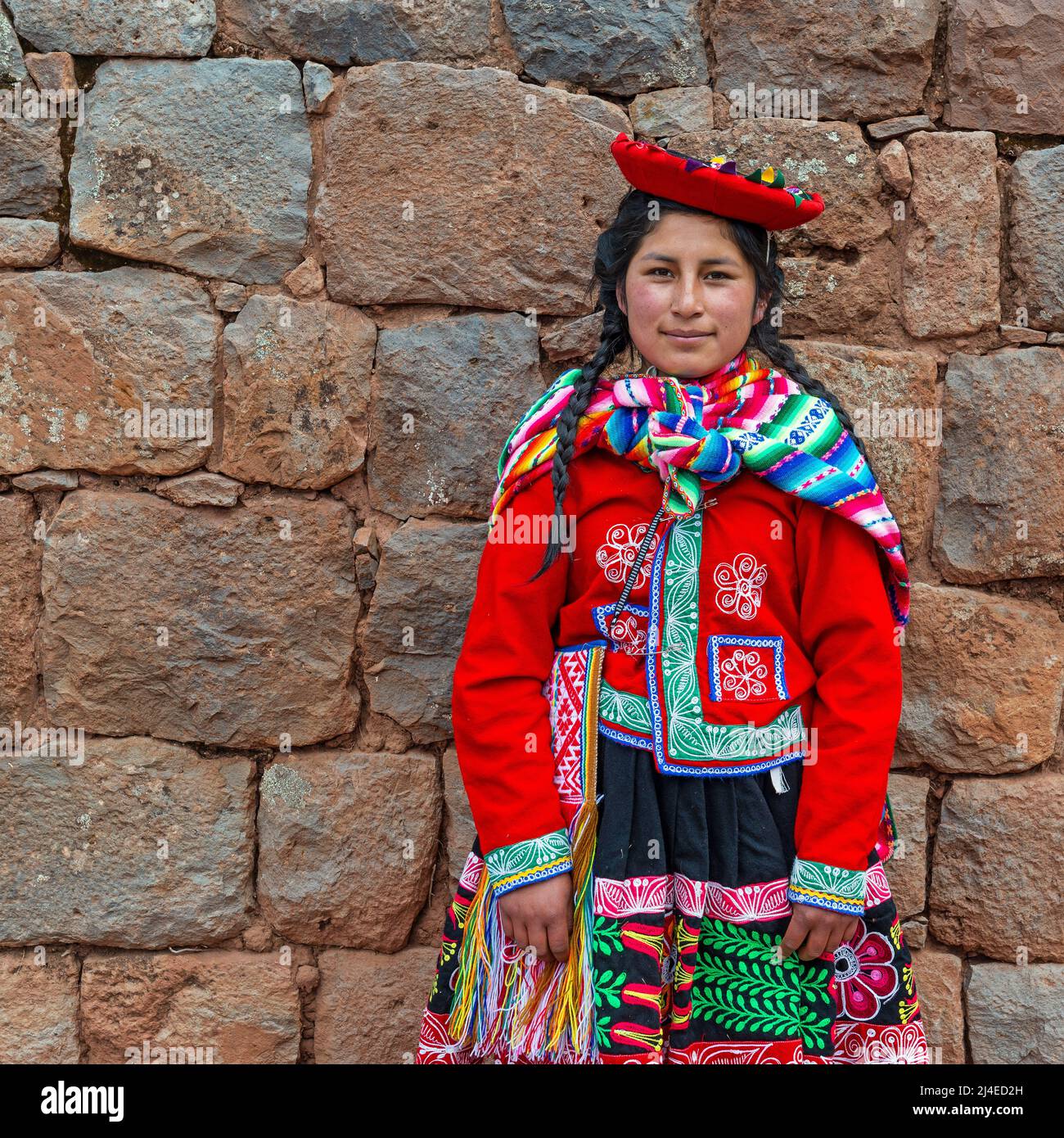 Portrait of young Peruvian indigenous Quechua woman with traditional textile clothing in front of Inca wall in Cusco, Sacred Valley of the Inca, Peru. Stock Photo