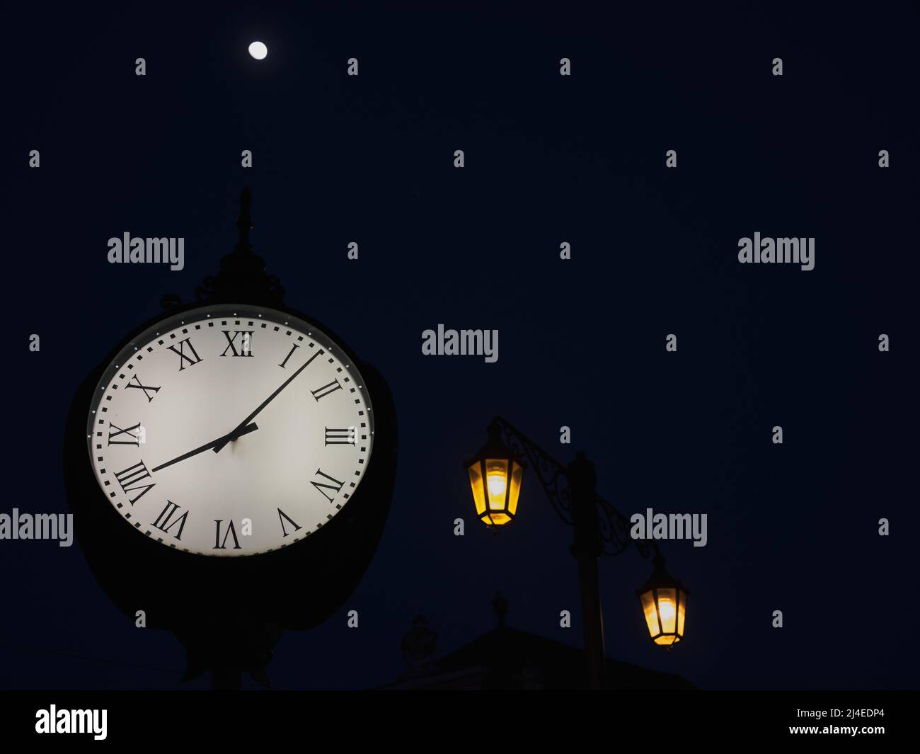 Historical clock, moon and glowing street lamps at night in Bratislava, Slovakia Stock Photo