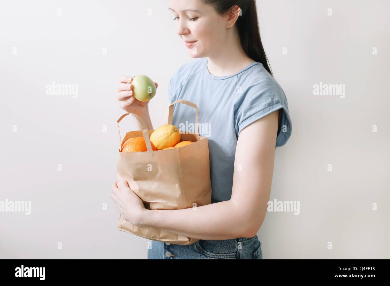 shopping, healthy eating and eco friendly concept - close up of woman holding eco bag with fruits on white background Stock Photo