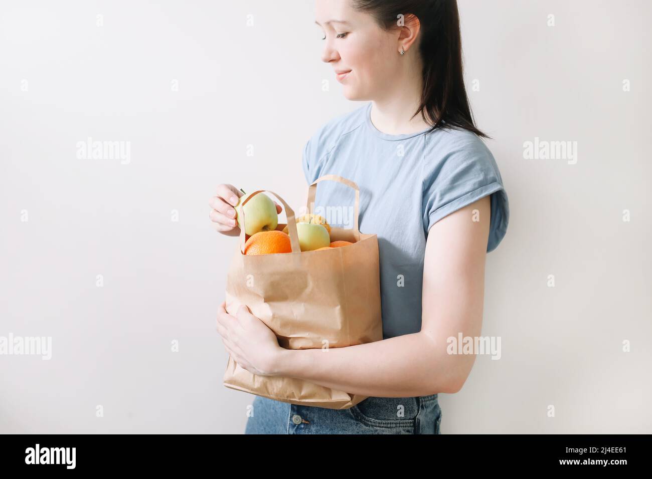 shopping, healthy eating and eco friendly concept - close up of woman holding eco bag with fruits on white background Stock Photo