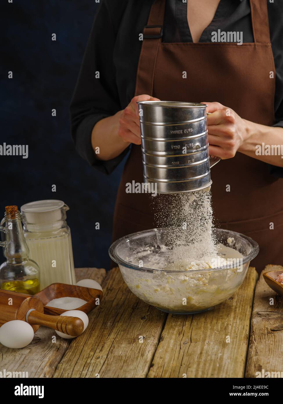 https://c8.alamy.com/comp/2J4EE9C/the-chef-prepares-the-dough-on-a-dark-background-sift-the-flour-through-a-sieve-into-a-large-glass-bowl-flour-in-frozen-flight-recipes-for-dough-pr-2J4EE9C.jpg