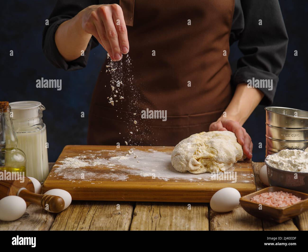 Professional chef kneads the dough on a wooden cutting board, dark