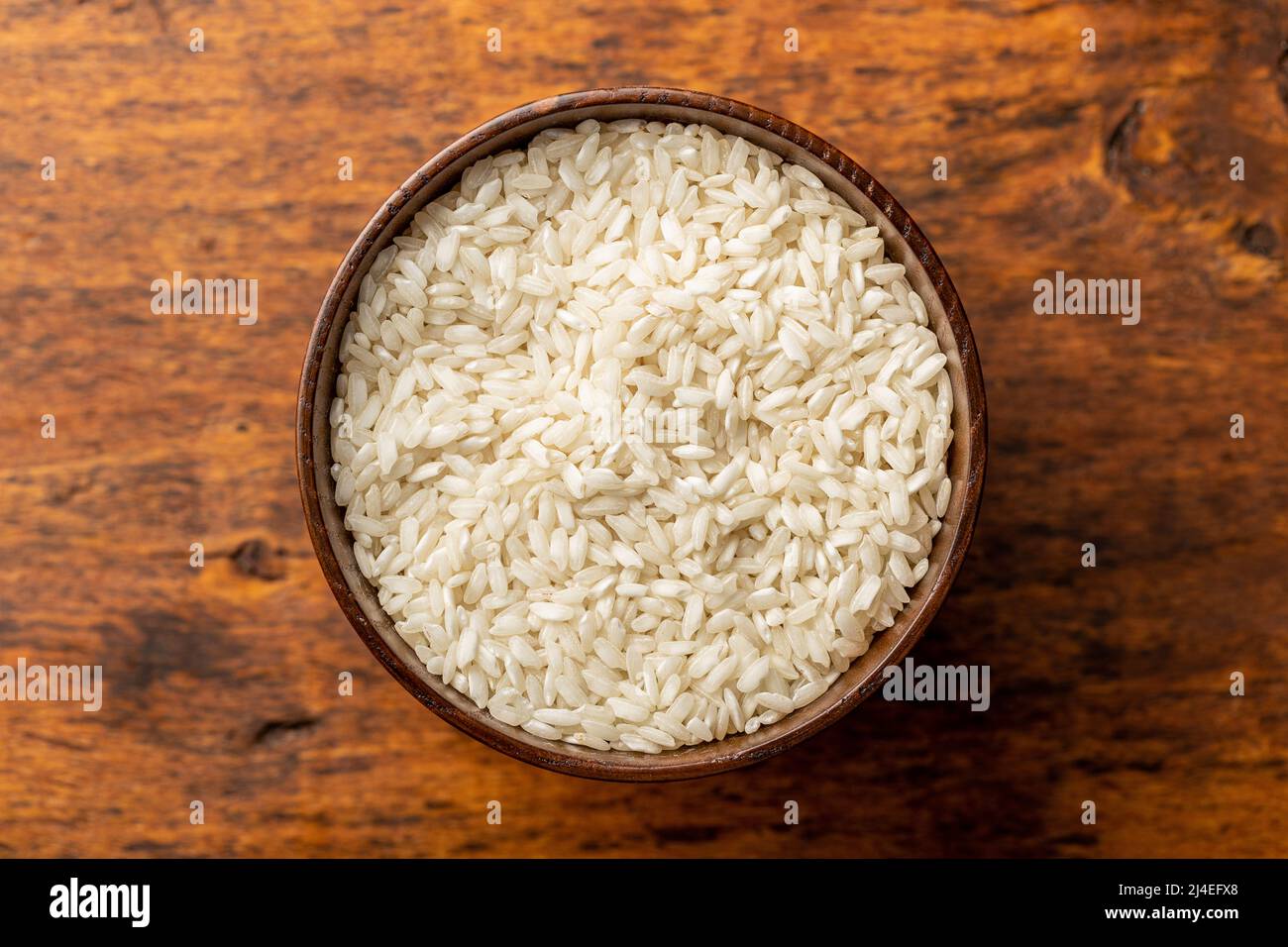 Uncooked Carnaroli risotto rice in bowl on a wooden table. Top view. Stock Photo