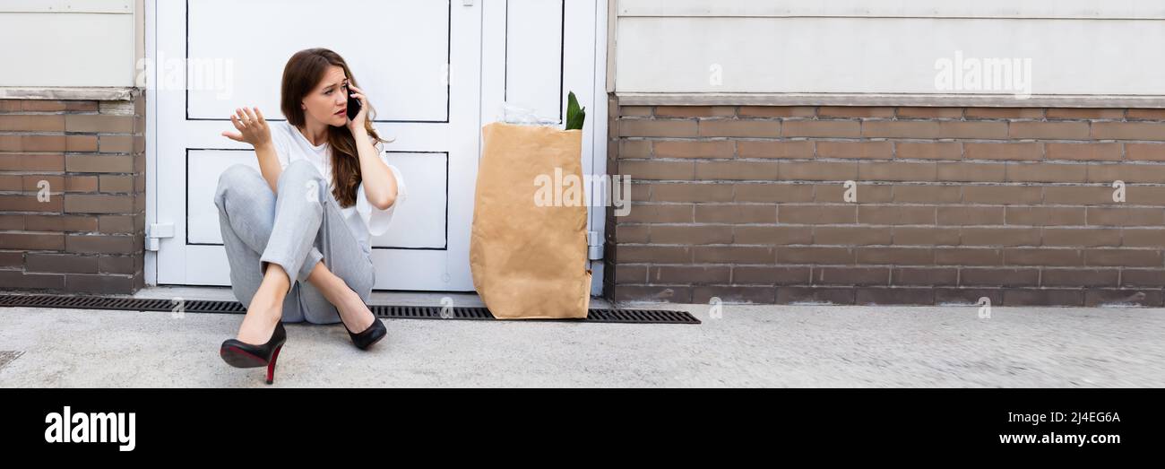 An Afraid Young Woman Sitting Outside The Door Talking On Mobile Phone Stock Photo