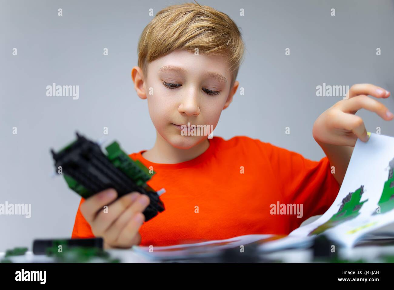 a boy plays with a plastic constructor examines the instructions for ...