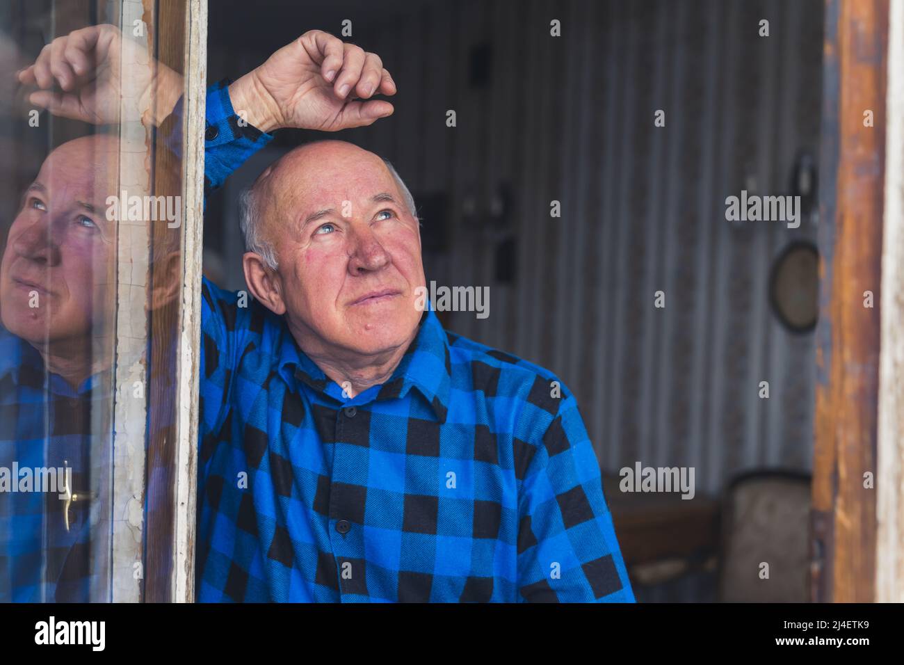 Pensive retired European man in his 80s looking up through the window and one hand in the air. High quality photo Stock Photo