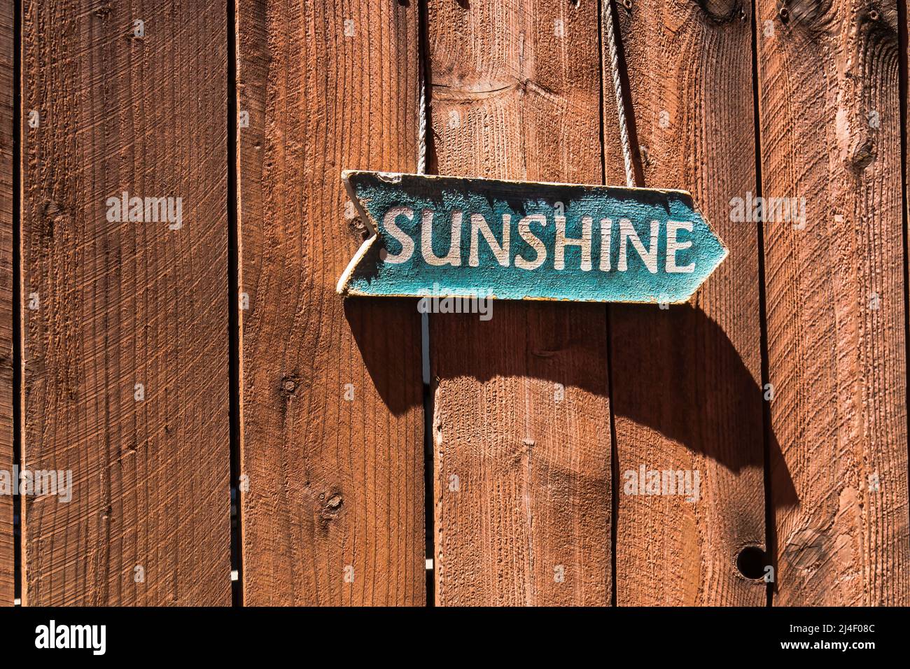 Old sunshine sign shaped like an arrow hanging on a redwood fence and casting a angular shadow from the afternoon light in Los Alamos, California. Stock Photo