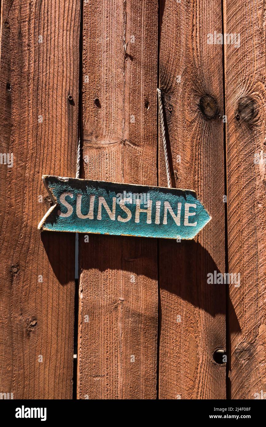Old sunshine sign shaped like an arrow hanging on a redwood fence and casting a angular shadow from the afternoon light in Los Alamos, California. Stock Photo