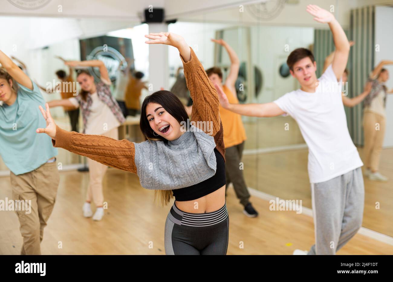 Happy brunette teenage girl practicing vigorous dance with group Stock Photo