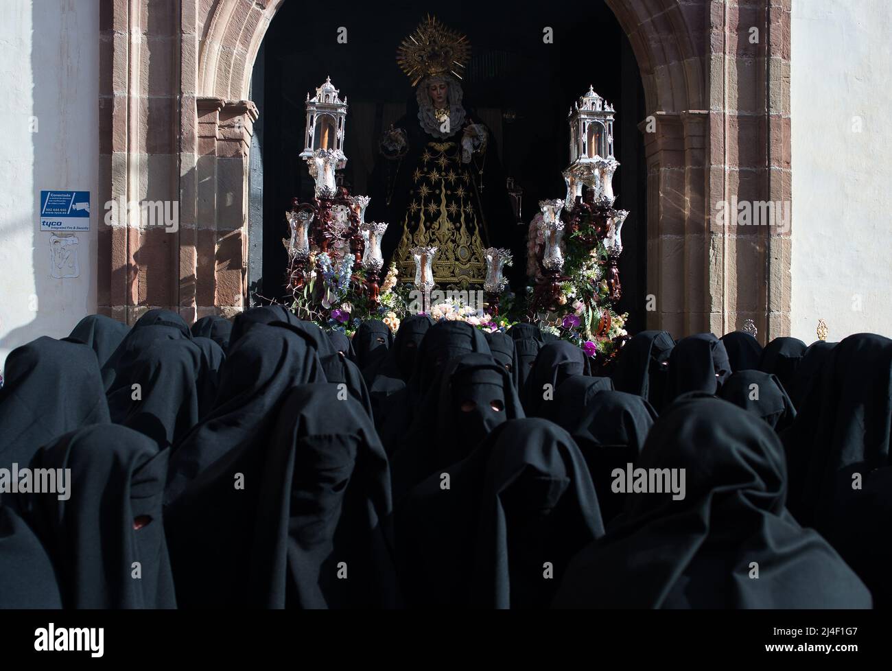 Penitents of “Santa Cruz” brotherhood covered with black hoods are seen carrying an ornate float
