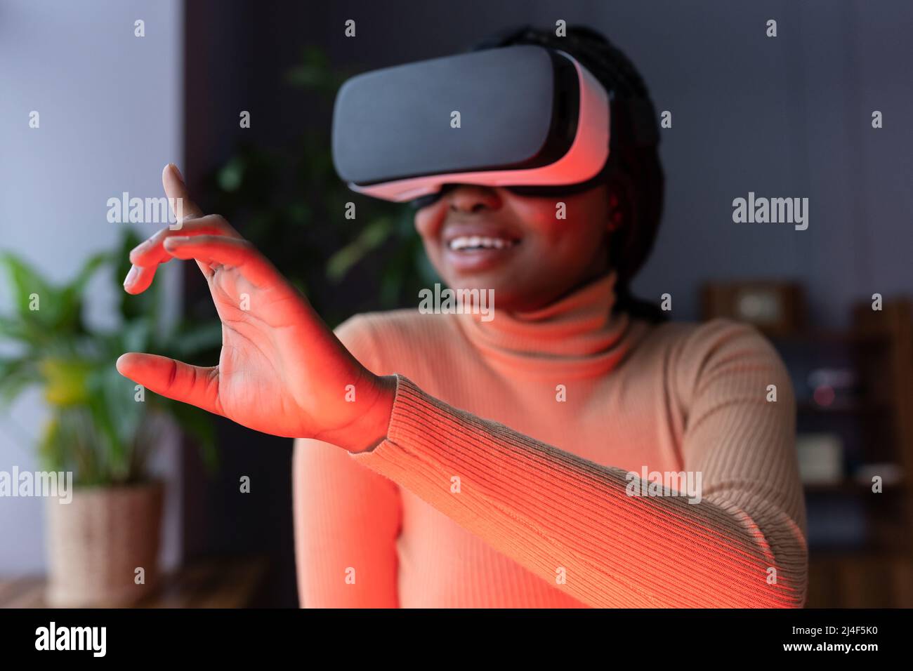 Joyful afro female touching virtual object with finger while working in virtual reality headset Stock Photo