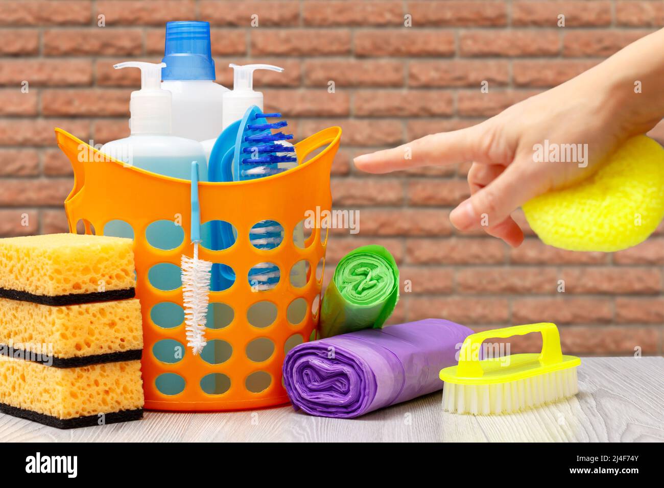 Plastic basket with bottles of dishwashing liquid, detergent for microwave ovens and stoves with female hand. Washing and cleaning concept. Stock Photo