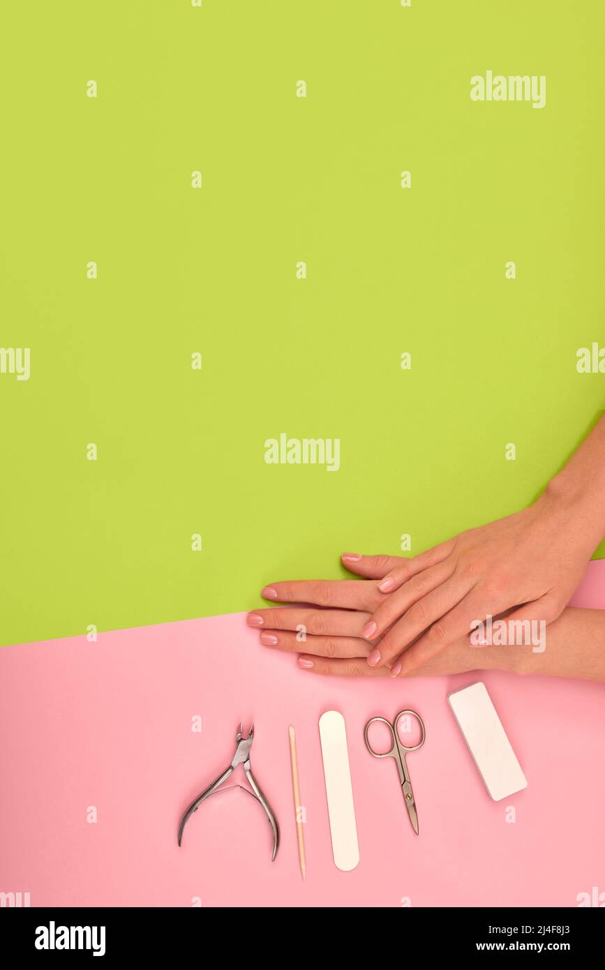 Hands with natural color manicure next to instruments for the procedure on green background Stock Photo