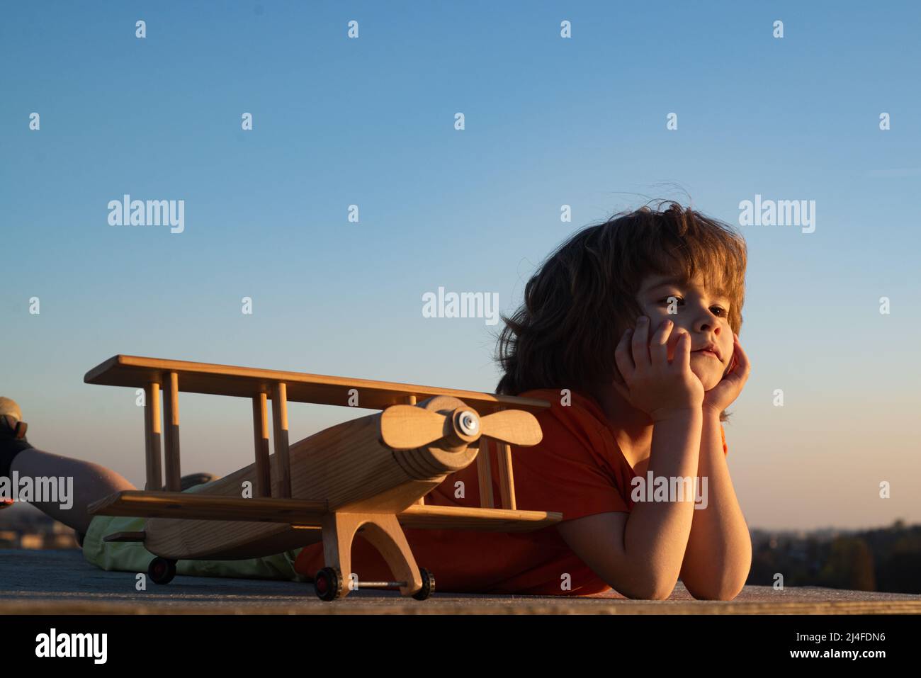 Little boy 7 year old with wooden plane, boy wants to become pilot and astronaut. Happy child play with toy airplane. Kids pilot dreams of flying. Stock Photo