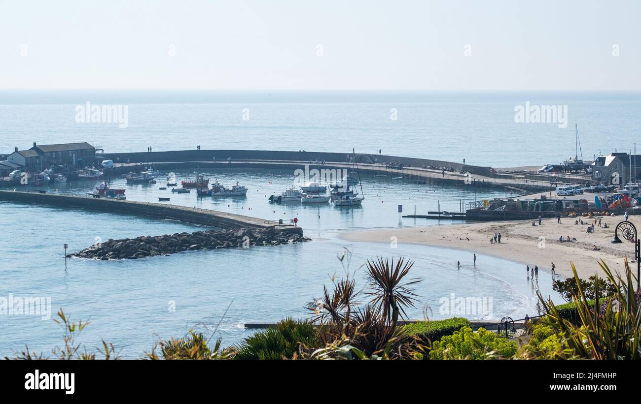 Spring sunshine upon the ancient stone pier, known as the Cobb, forming the harbour at Lyme Regis and upon the adjacent beach on the Jurassic coast UK Stock Photo