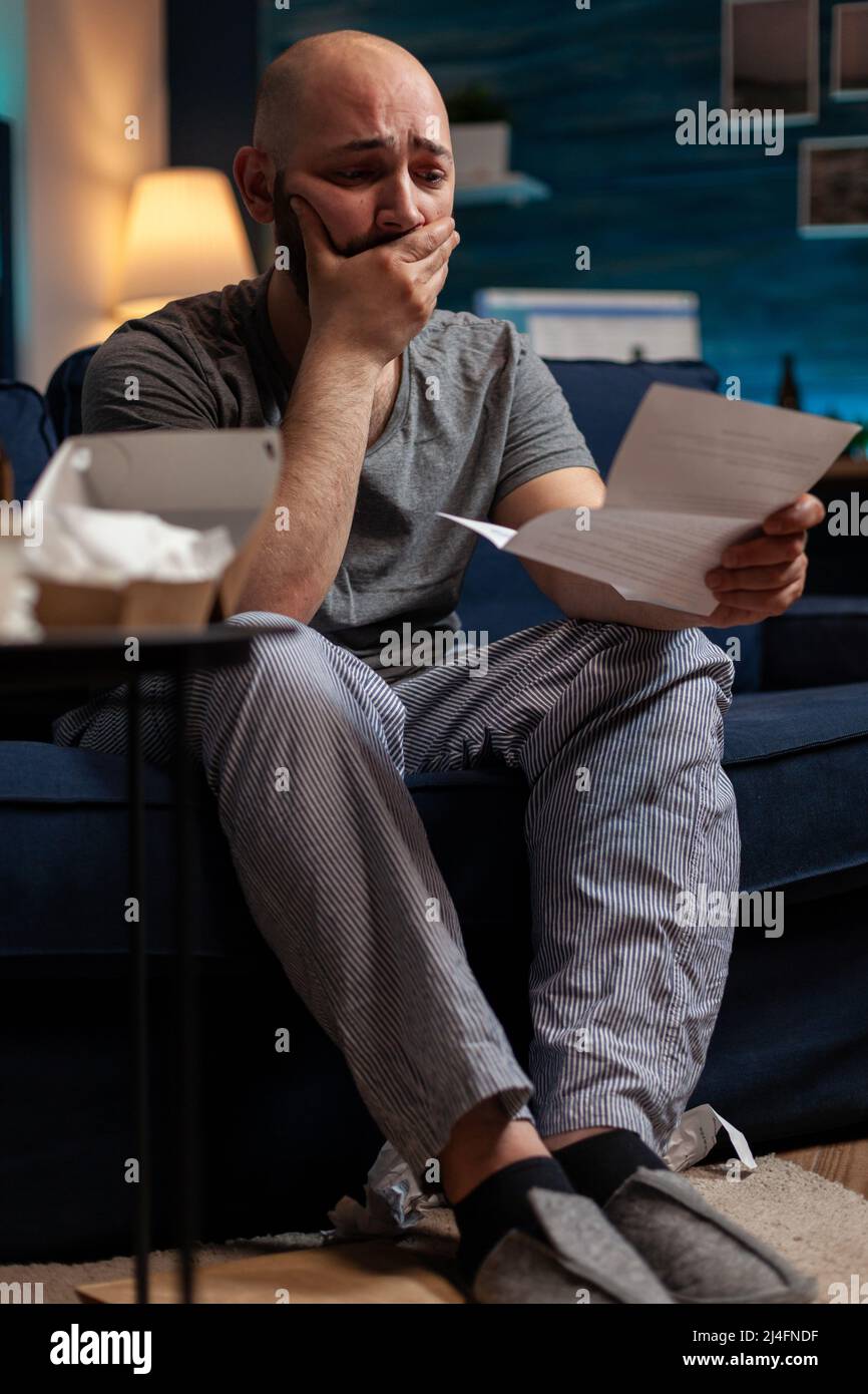 Desperate frustrated adult worrying about eviction notice letter, feeling sad about financial crisis. Anxious man with chronic depression having to pay taxes, reading bank warning paper. Stock Photo