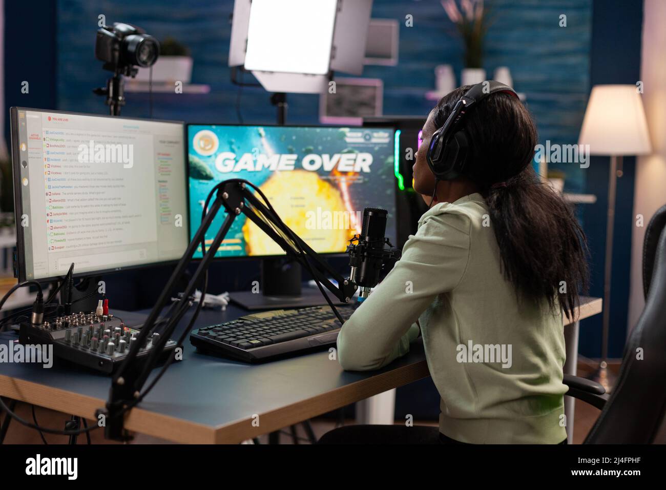 Sad nervous pro gamer sitting at gaming desk playing space shooter videogames losing online games championship. Upset esport woman streaming live using RGB computer equipment, Game over on screen Stock Photo
