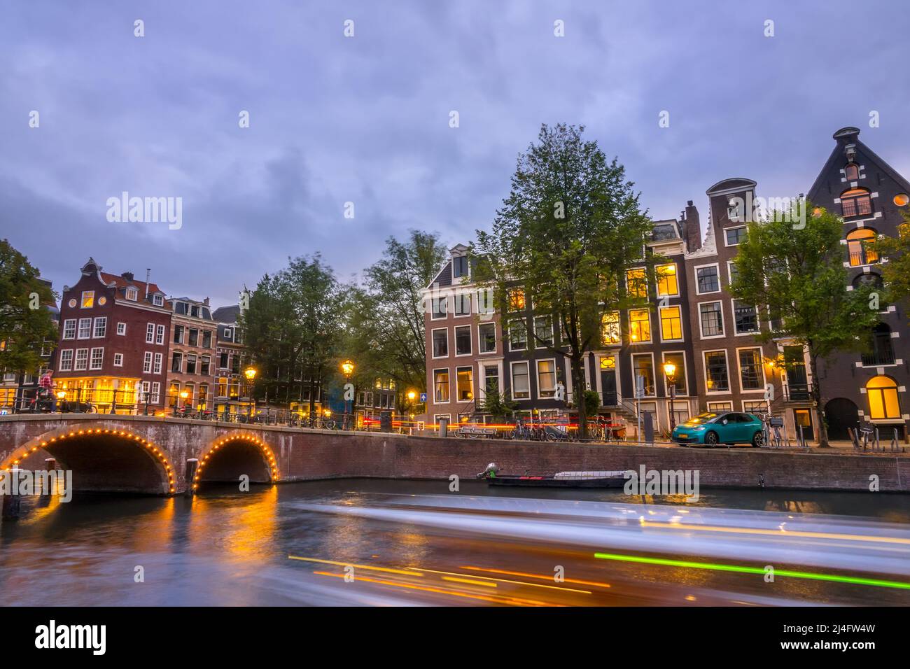 Netherlands. Evening on the Amsterdam canal. Old stone bridge and typical houses on the embankment. Traffic on the water and streets Stock Photo