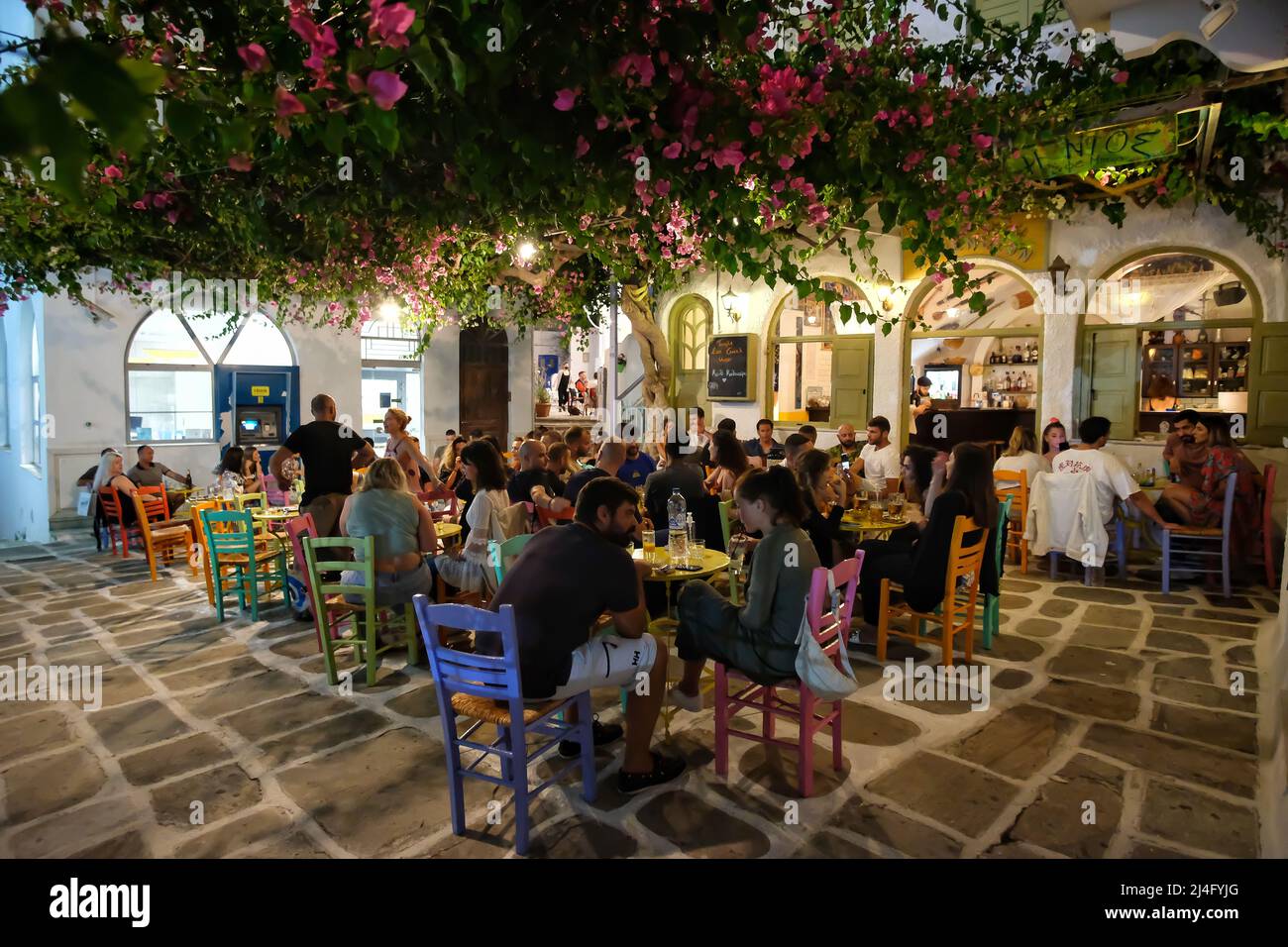 Ios, Greece - June 13, 2021 : Tourists enjoying drinks and listening to live greek music at a picturesque and colorful outdoor bar in iOS Stock Photo