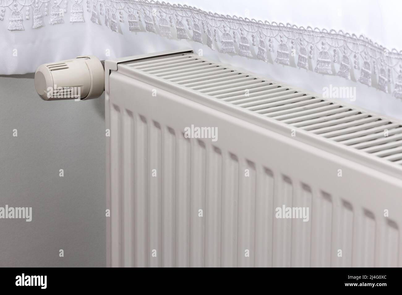 Corrugated white heating radiator and temperature knob. Heater controller in selective focus. Stock Photo