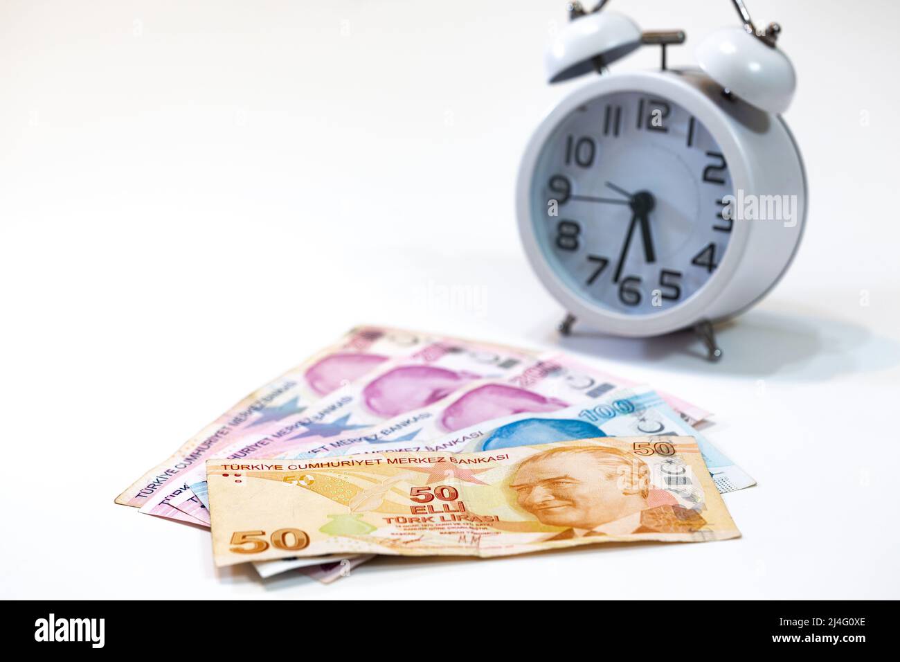 50, 100 and 200 Turkish banknotes and alarm clock on isolated white background. 50 Turkish lira in selective focus. Time is money concept. Stock Photo