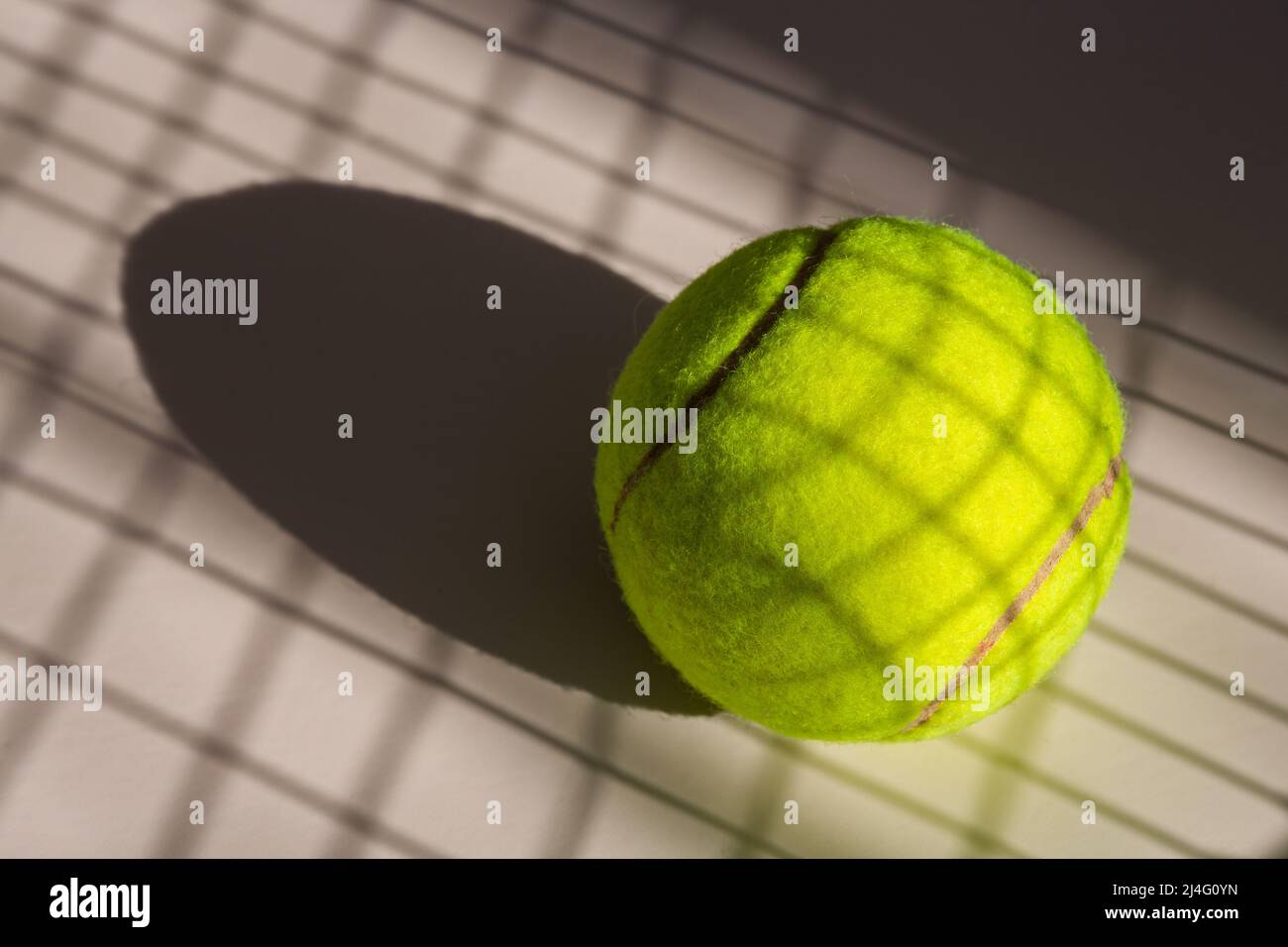 Tennis ball and its shadow on an isolated white background. Tennis ball has shadow of tennis racket net on it. Stock Photo