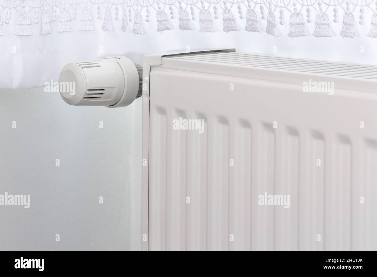 White heating radiator and temperature knob. Heater controller in selective focus. Stock Photo