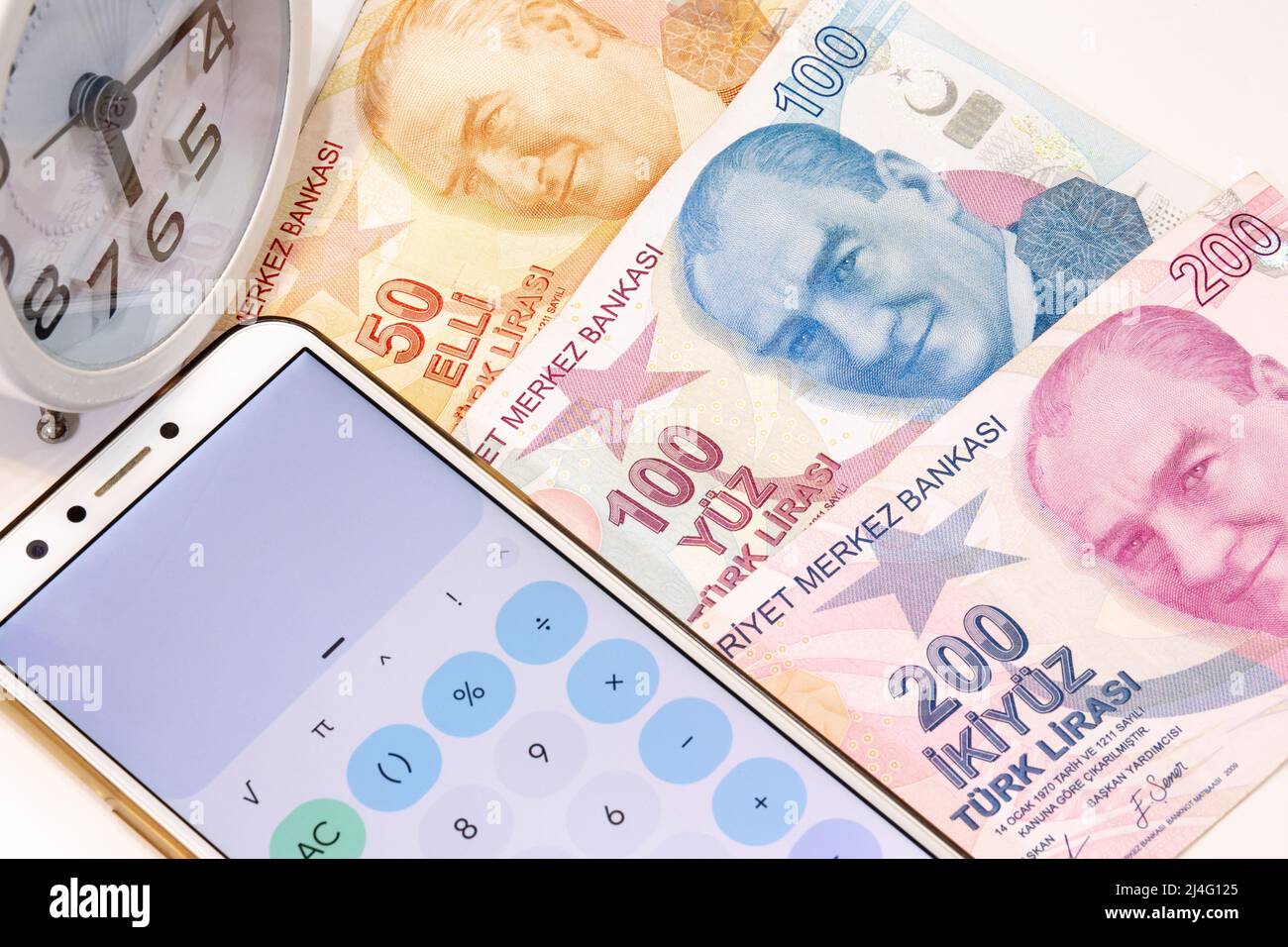 50, 100 and 200 turkish banknotes, alarm clock and calculator app open mobile phone on isolated background.Banknotes in selective focus. Time is money Stock Photo
